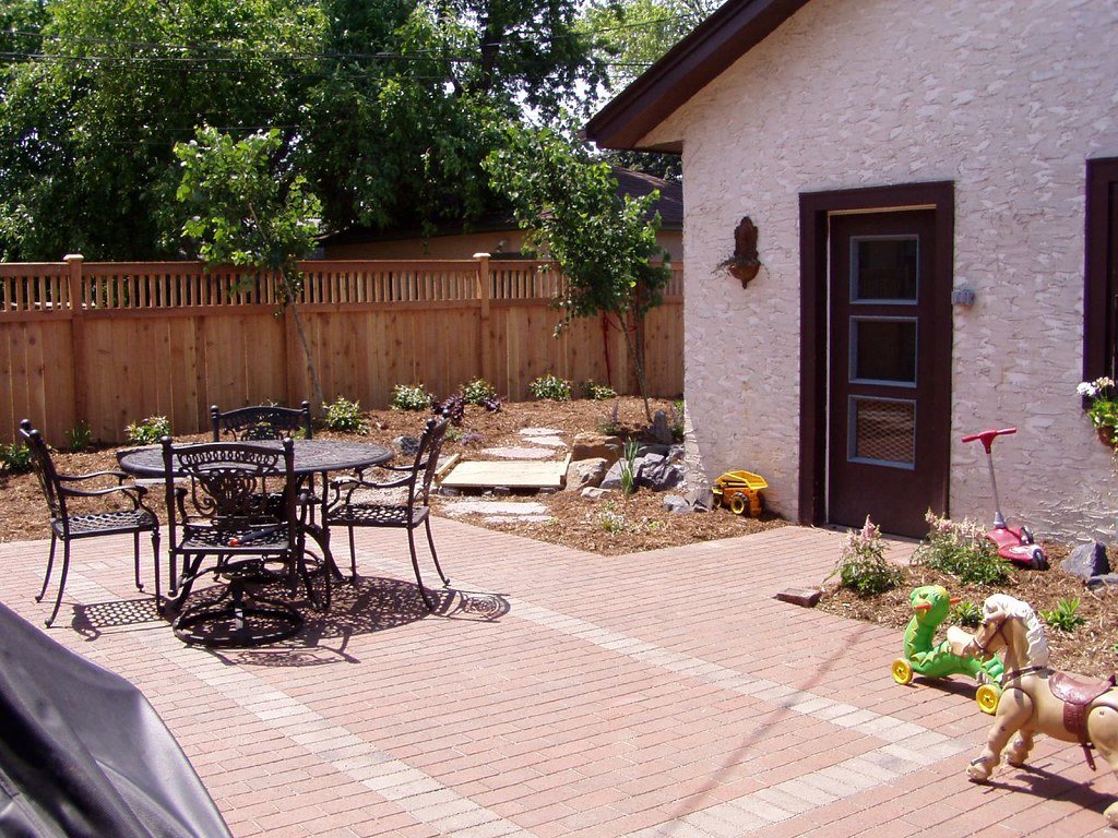 A finished paver patio laid in a backyard with a seating area beside planting beds